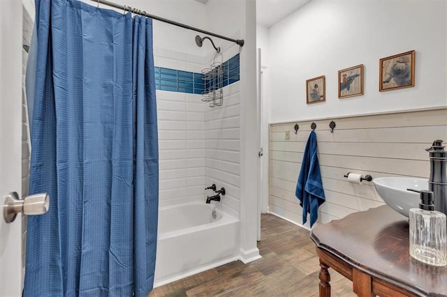 full bathroom featuring wood finished floors, shower / bath combo with shower curtain, wainscoting, a sink, and wood walls