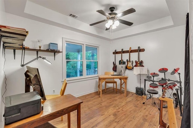 office space with a tray ceiling, ceiling fan, light wood-style flooring, and baseboards