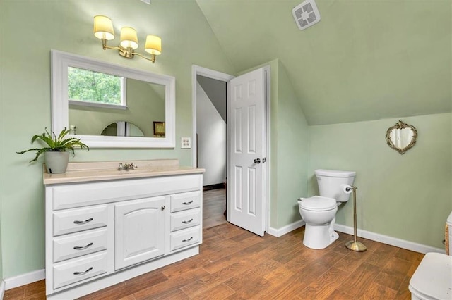 bathroom featuring lofted ceiling, toilet, vanity, wood finished floors, and baseboards