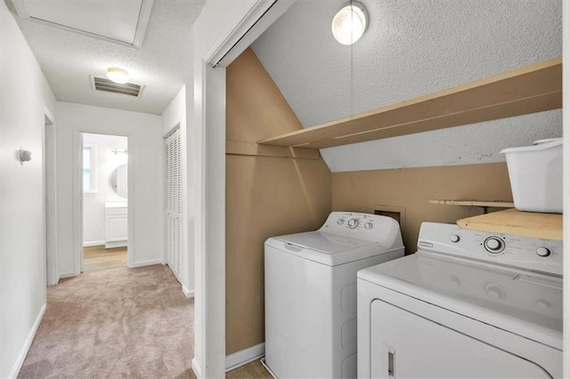 clothes washing area with washer and clothes dryer, light colored carpet, a textured ceiling, and baseboards