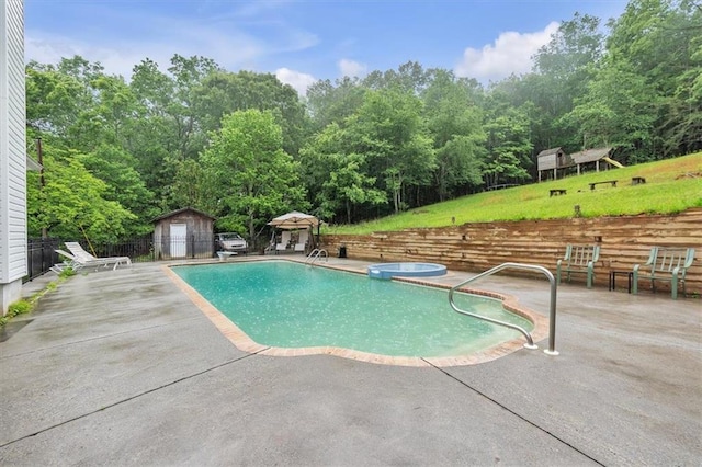 view of swimming pool with a patio area, fence, an outbuilding, a pool with connected hot tub, and a storage shed