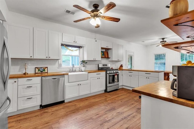 kitchen featuring appliances with stainless steel finishes, a sink, ceiling fan, wood counters, and tasteful backsplash