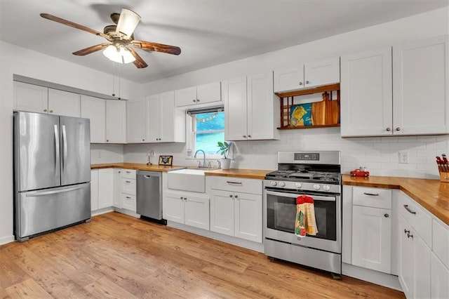 kitchen with stainless steel appliances, a sink, butcher block counters, ceiling fan, and decorative backsplash
