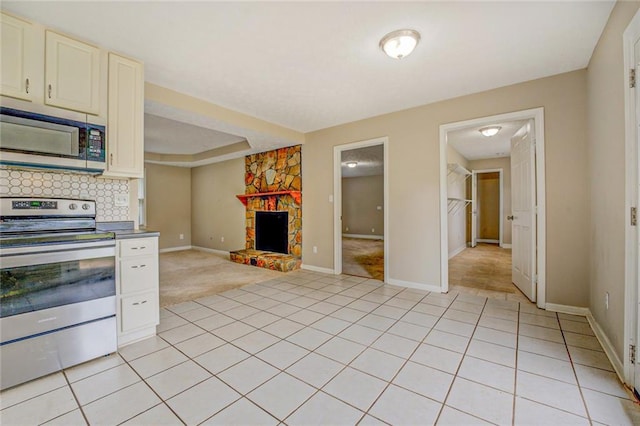 kitchen with tasteful backsplash, a stone fireplace, light tile patterned floors, and appliances with stainless steel finishes