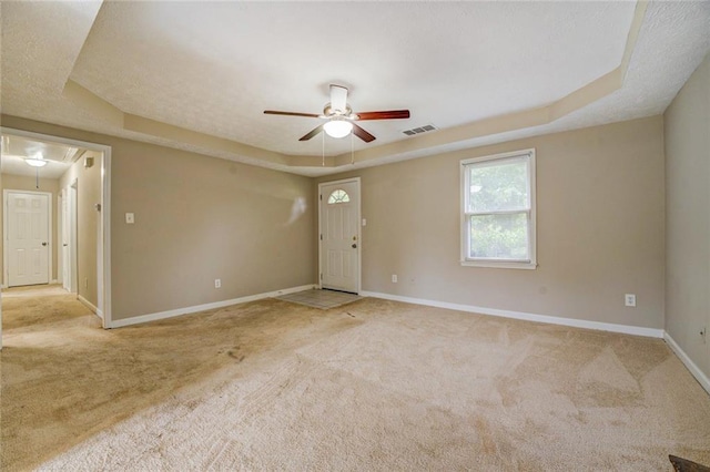 empty room featuring ceiling fan, a raised ceiling, and light colored carpet