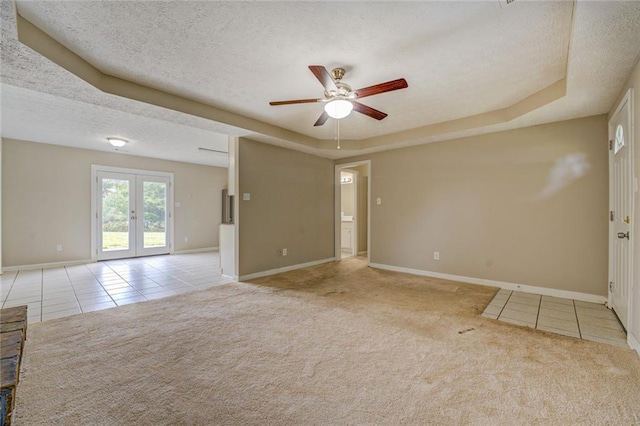 carpeted spare room with french doors, a textured ceiling, a raised ceiling, and ceiling fan