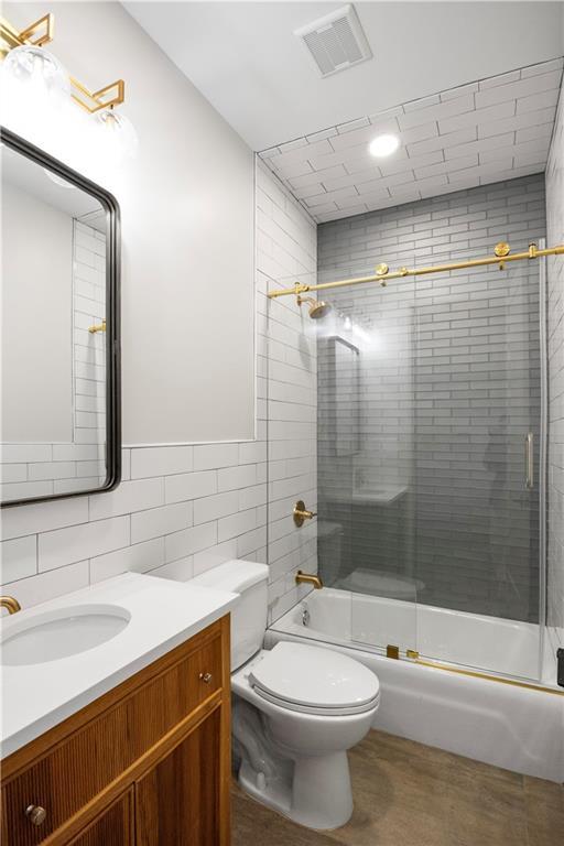 full bathroom featuring combined bath / shower with glass door, vanity, toilet, and tile walls