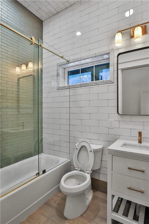 full bathroom with hardwood / wood-style floors, bath / shower combo with glass door, toilet, vanity, and tile walls