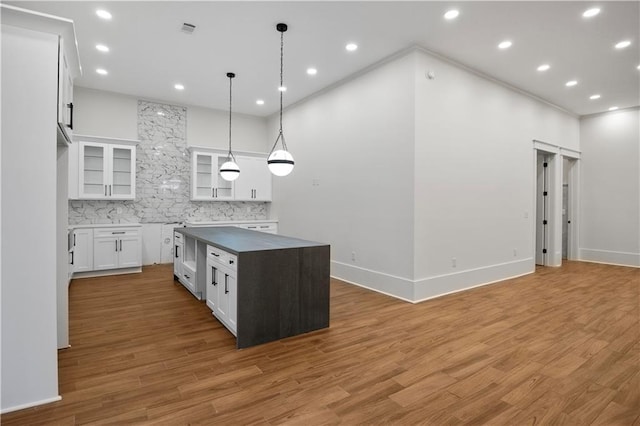 kitchen with pendant lighting, white cabinets, decorative backsplash, a kitchen island, and wood-type flooring