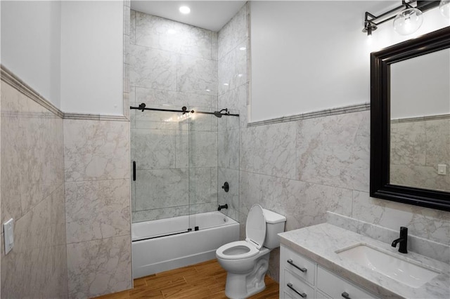 full bathroom with combined bath / shower with glass door, hardwood / wood-style floors, toilet, vanity, and tile walls