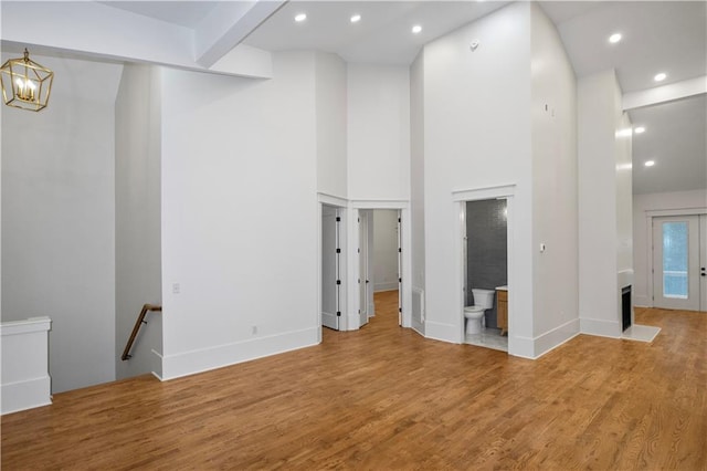 unfurnished living room featuring beam ceiling, wood-type flooring, a towering ceiling, and a chandelier