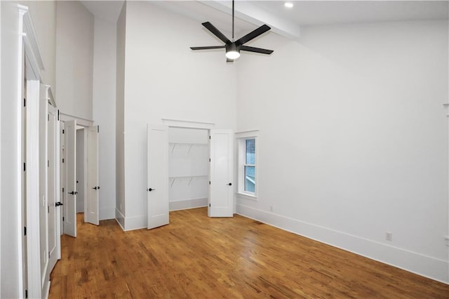 unfurnished bedroom with beamed ceiling, ceiling fan, wood-type flooring, and high vaulted ceiling