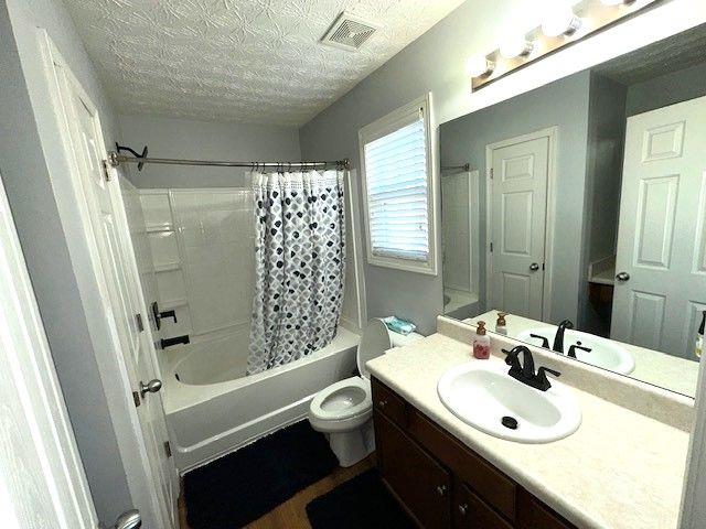 full bathroom with a textured ceiling, toilet, vanity, and shower / bath combination with curtain