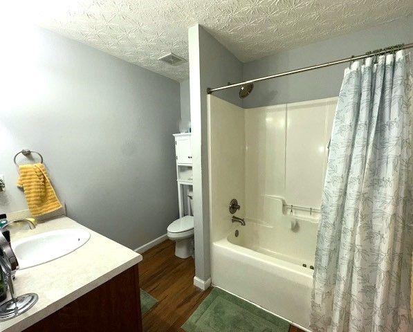 full bathroom with wood-type flooring, shower / tub combo, a textured ceiling, toilet, and vanity