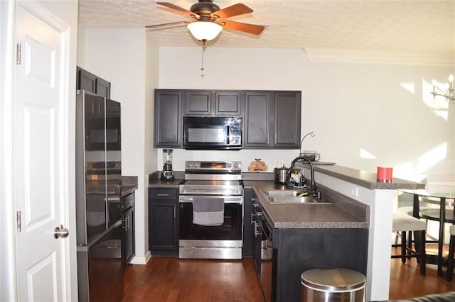 kitchen with a textured ceiling, appliances with stainless steel finishes, sink, dark hardwood / wood-style floors, and kitchen peninsula