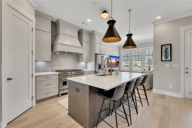 kitchen with a breakfast bar, custom exhaust hood, decorative light fixtures, premium appliances, and a kitchen island with sink