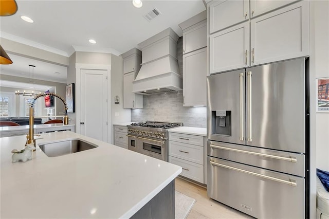 kitchen with sink, backsplash, premium appliances, custom exhaust hood, and a center island with sink