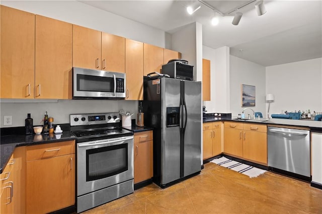 kitchen with sink, dark stone counters, track lighting, light tile patterned floors, and appliances with stainless steel finishes