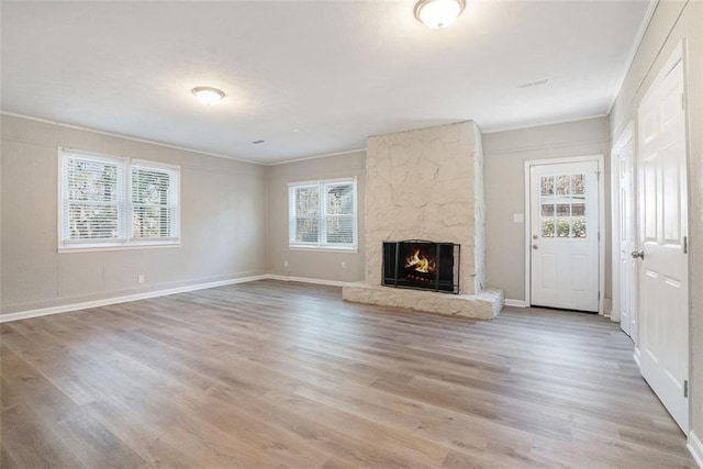 unfurnished living room featuring a stone fireplace, hardwood / wood-style floors, and ornamental molding