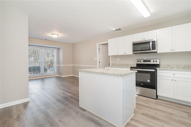 kitchen featuring white cabinetry, stainless steel appliances, light stone counters, a kitchen island, and light wood-type flooring