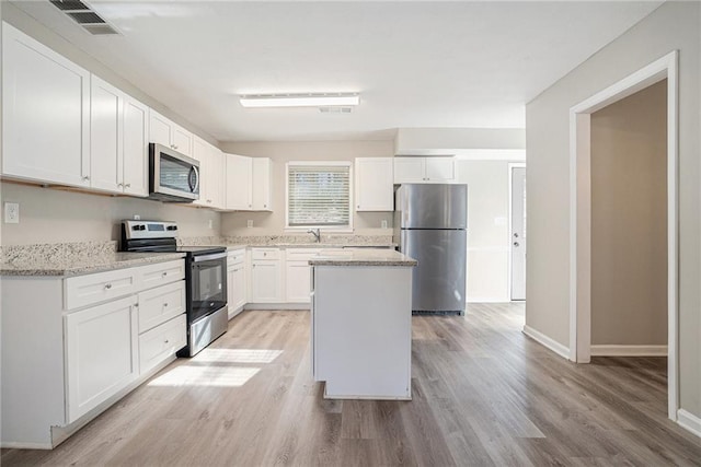 kitchen featuring light stone counters, white cabinetry, stainless steel appliances, and light hardwood / wood-style flooring