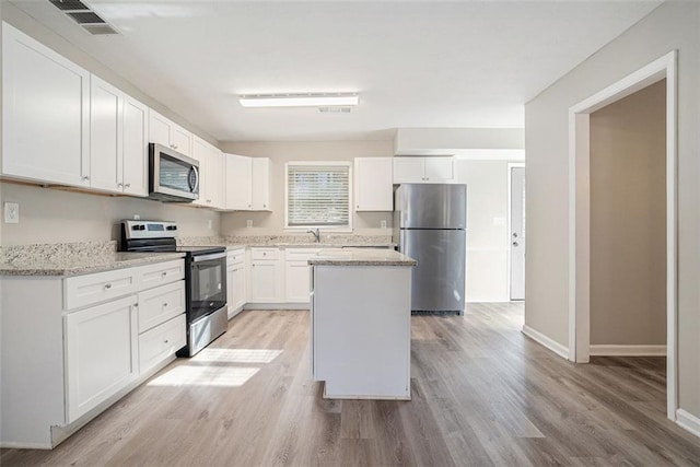 kitchen featuring appliances with stainless steel finishes, light stone counters, light hardwood / wood-style flooring, white cabinets, and a kitchen island