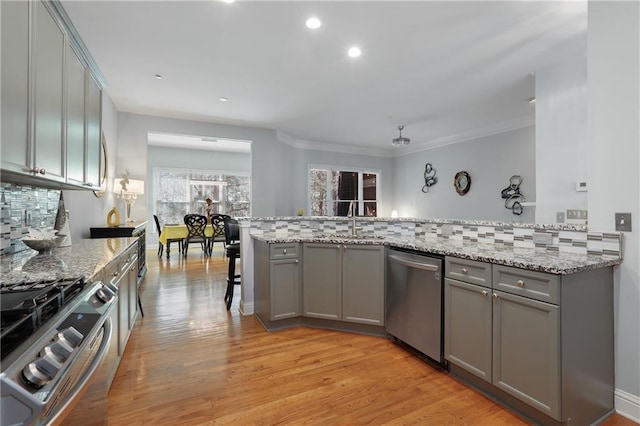 kitchen with light wood finished floors, stainless steel appliances, tasteful backsplash, gray cabinetry, and a sink