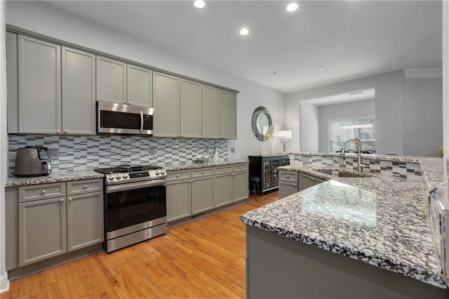 kitchen featuring tasteful backsplash, stainless steel appliances, gray cabinetry, light wood-type flooring, and a sink