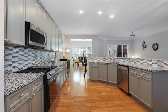 kitchen featuring tasteful backsplash, gray cabinets, appliances with stainless steel finishes, light wood-style floors, and a sink