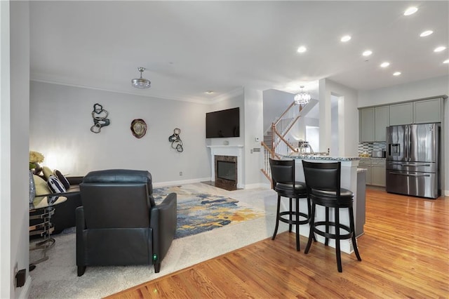 living area with a fireplace, light wood finished floors, stairway, ornamental molding, and baseboards