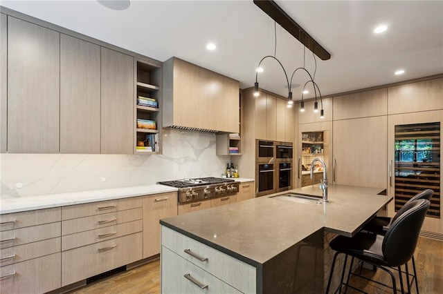 kitchen with light brown cabinetry, appliances with stainless steel finishes, a sink, wood finished floors, and beverage cooler