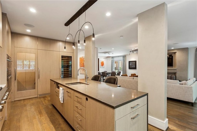 kitchen with light brown cabinets, open floor plan, a sink, and dark wood finished floors