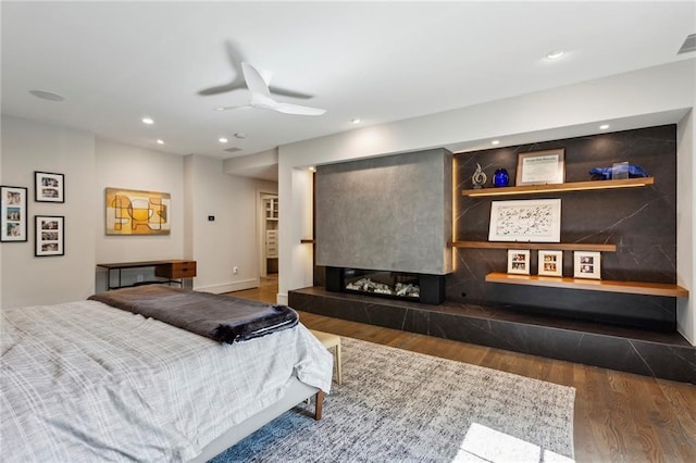 bedroom featuring visible vents, a ceiling fan, a tiled fireplace, wood finished floors, and recessed lighting