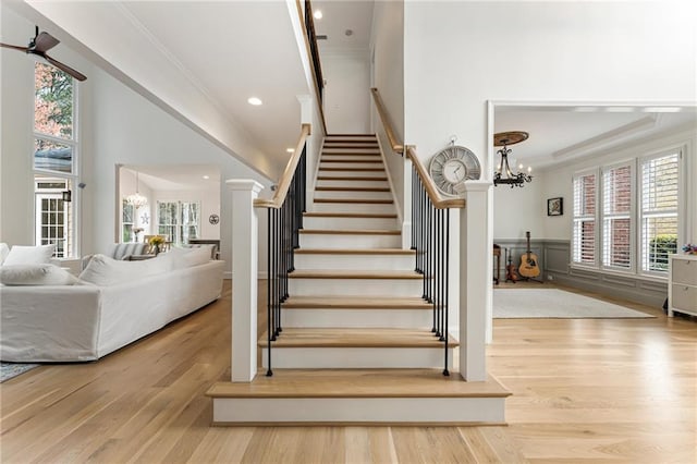 stairway featuring wood finished floors, ornamental molding, and an inviting chandelier