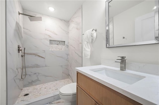 bathroom with a tile shower, vanity, and toilet