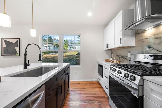 kitchen with light stone countertops, sink, wall chimney exhaust hood, white cabinets, and appliances with stainless steel finishes