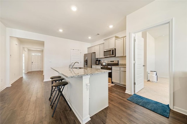 kitchen featuring dark wood finished floors, a breakfast bar, a kitchen island with sink, stainless steel appliances, and a sink