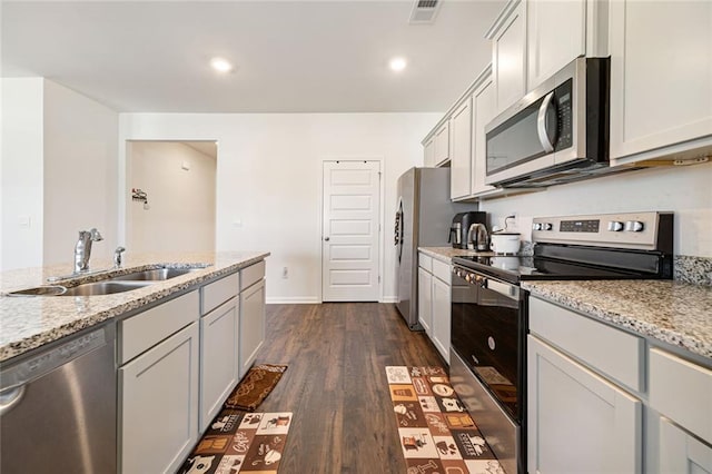 kitchen featuring light stone counters, stainless steel appliances, a sink, visible vents, and dark wood finished floors