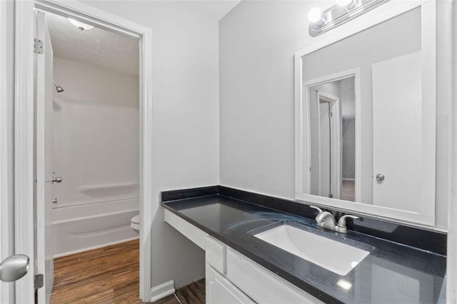 full bathroom featuring washtub / shower combination, hardwood / wood-style floors, a textured ceiling, toilet, and vanity