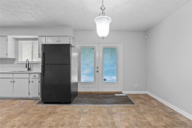 kitchen featuring pendant lighting, french doors, white cabinets, black refrigerator, and sink