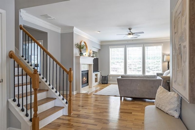 4765 Silver Leaf Dr, Cumming, GA 30040 - living room with a glass covered fireplace, ceiling fan, light wood-style flooring, ornamental molding, and stairs
