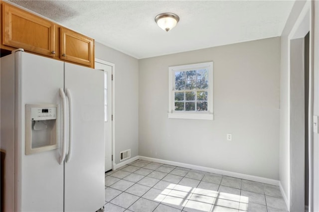 kitchen with light tile patterned flooring, a textured ceiling, and white fridge with ice dispenser