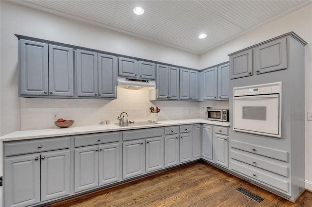 kitchen with cooktop, tasteful backsplash, dark hardwood / wood-style floors, oven, and gray cabinets