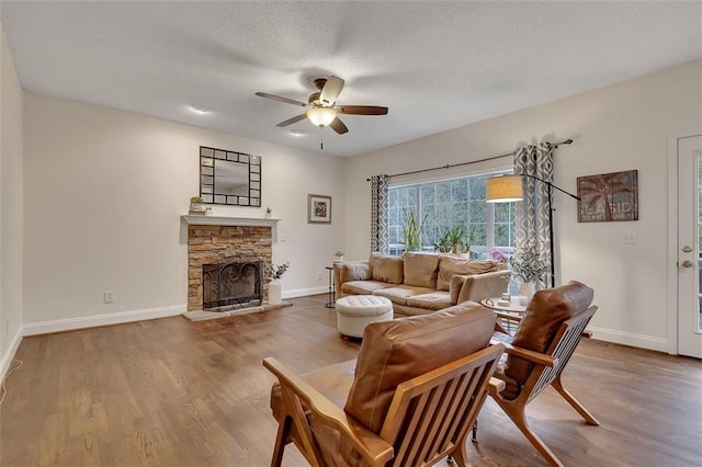 living room with wood-type flooring, a textured ceiling, a stone fireplace, and ceiling fan