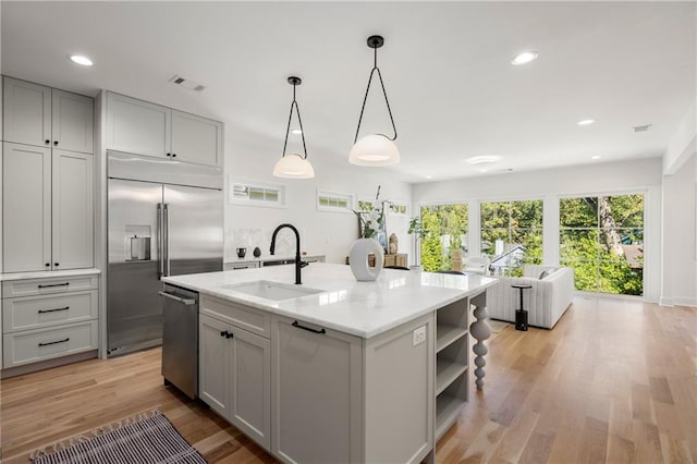 kitchen featuring a center island with sink, light wood-type flooring, stainless steel appliances, pendant lighting, and sink