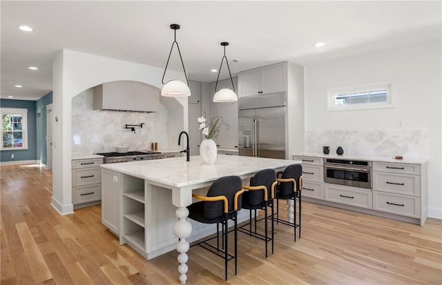 kitchen featuring tasteful backsplash, a center island with sink, light hardwood / wood-style flooring, pendant lighting, and stainless steel appliances