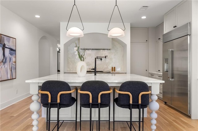 kitchen with white cabinets, decorative backsplash, stainless steel built in refrigerator, hanging light fixtures, and light wood-type flooring