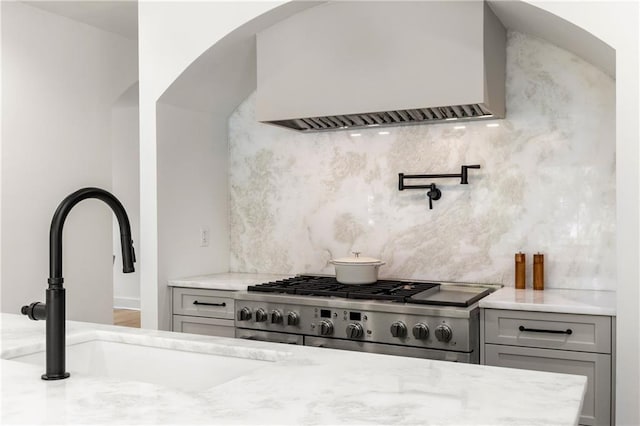 kitchen with gray cabinetry, tasteful backsplash, sink, stainless steel stove, and custom range hood