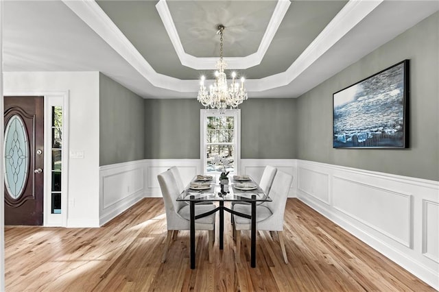 dining room featuring a raised ceiling, a notable chandelier, wood finished floors, and wainscoting