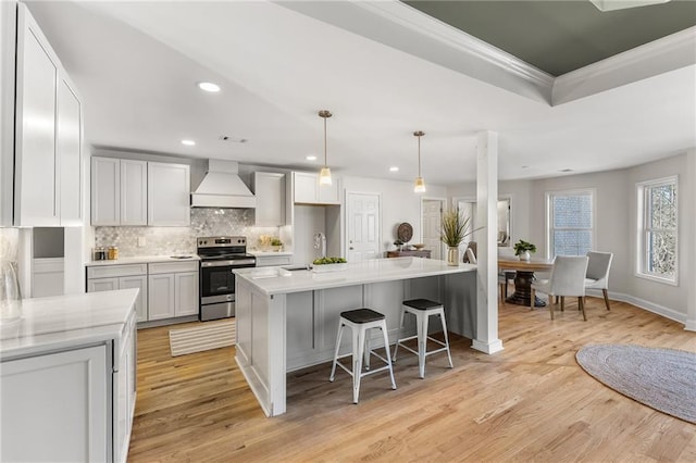 kitchen featuring custom range hood, tasteful backsplash, stainless steel electric stove, light wood-style floors, and light countertops
